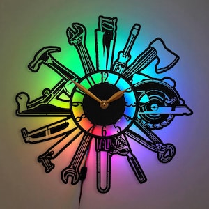 Könnte beinhalten: Eine schwarze und goldene Uhr mit einem Regenbogen-LED-Lichtring. Das Zifferblatt der Uhr ist von verschiedenen Werkzeugen umgeben, darunter ein Hammer, eine Säge, ein Schraubenschlüssel und ein Schraubendreher.