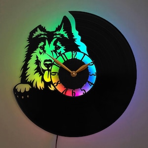 Può includere: Un orologio in vinile nero con un design arcobaleno colorato. L'orologio presenta una silhouette di una testa di cane con la bocca aperta, come se stesse mordendo il quadrante dell'orologio.