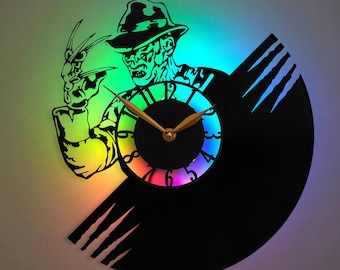 May include: A black vinyl record clock featuring a silhouette of Freddy Krueger from the Nightmare on Elm Street movie franchise. The clock face is a rainbow color and the clock hands are gold. The record is mounted on a black wall mount.