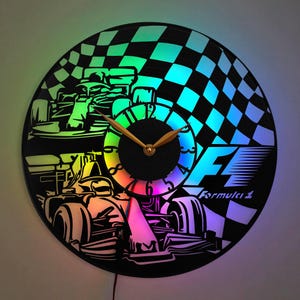 May include: A black vinyl record clock with a Formula 1 race car design. The clock face is a rainbow of colors and the clock hands are gold. The clock has a black background with a checkered flag design.