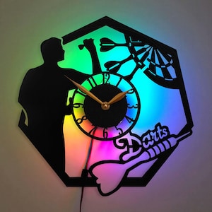 May include: A black silhouette of a person throwing a dart at a dartboard with a clock face in the center. The background is a rainbow of colors. The words "Darts" are written on the bottom right of the image.