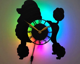 May include: A black silhouette of a poodle with a clock face in the center of its body. The clock face has rainbow colored numbers and a gold hour and minute hand. The background is a gradient of rainbow colors.