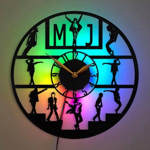 May include: A black vinyl record clock with a rainbow LED light display. The clock features a silhouette of Michael Jackson in different poses. The clock face has a gold-colored clock hand and the text "MJ" is displayed at the top.