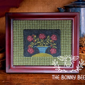 Könnte beinhalten: Ein gerahmtes Blumenkunstwerk mit schwarzem Hintergrund und einer blauen Vase mit roten Rosen. Der Rahmen ist dunkelrot und der Hintergrund ein grün-schwarzes Karomuster. Das Kunstwerk ist mit "THE BONNY BEE" signiert.