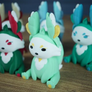 An angled close-up shot focused on the Spring Flutterfox miniature, featuring its mint green, white, and yellow colors. It sits on a wooden table, with other blurred Flutterfox figures, including the teal Summer fox, flanking it.