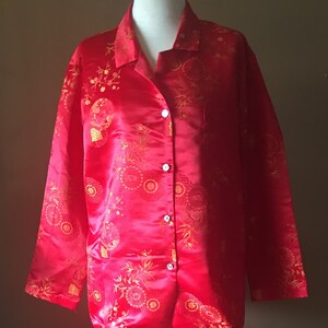 May include: Red pajama set with a gold floral pattern. The set includes a button-down shirt and matching pants. The fabric has a satin sheen. The pajamas are displayed on a mannequin.