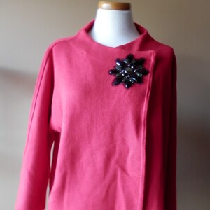 May include: A pink cardigan with a black jeweled flower brooch.