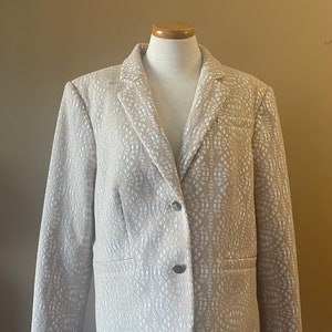 May include: A beige blazer with a white patterned design. The blazer has a notched collar, two button closure, and long sleeves.