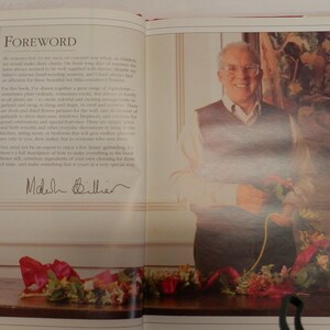 May include: A man in a brown sweater and glasses holds a bouquet of flowers. The text "Foreword" is visible in the background. The man is smiling and looking at the camera. The text "Madelyn  Biller" is signed in black ink.