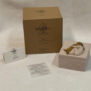 Könnte beinhalten: Eine hellbeige Willow Tree Andenkenbox mit Deckel, der ein Kind und einen Hund zeigt. Die Box hat einen Pfotenabdruck an der Seite. Ein brauner Karton und eine kleine Karte mit Text sind ebenfalls vorhanden.