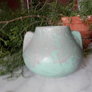 以下が含まれることがあります： 2つの取っ手が付いた、緑と灰色の小さな陶器の花瓶。花瓶は、まだら模様の釉薬がかけられており、丸みを帯びた形をしています。