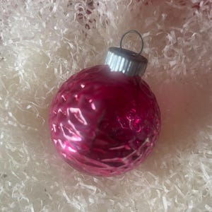 May include: A pink glass Christmas ornament with a textured surface and a silver top.
