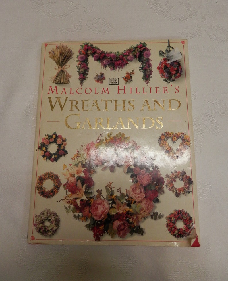 May include: Book cover featuring a colorful wreath of flowers and greenery. The title is "Malcolm Hillier's Wreaths and Garlands" with a DK logo.