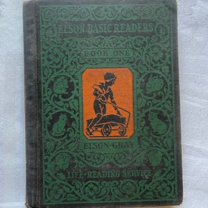 Könnte beinhalten: Ein altes grünes und schwarzes Buch mit einer orangefarbenen Illustration eines Kindes, das einen Wagen schiebt. Der Buchtitel lautet "Elson Basic Readers Book One" und der Verlag ist "Elson-Gray Life Reading Service".