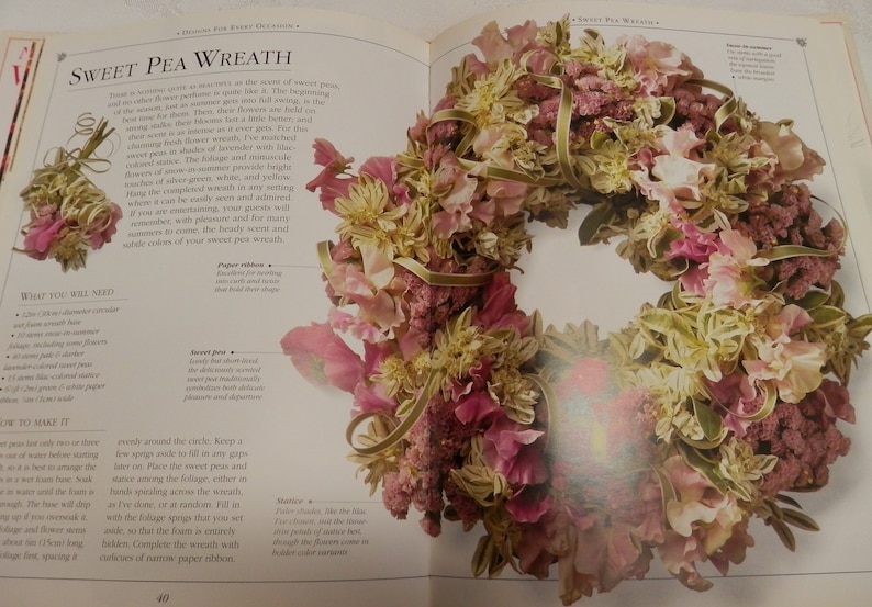 May include: A sweet pea wreath made with pink, white, and green flowers. The wreath is tied with a gold ribbon and is surrounded by text that says "Sweet Pea Wreath".
