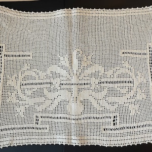 May include: A white crocheted doily with a floral design in the center. The doily has a square shape and a delicate lace pattern.