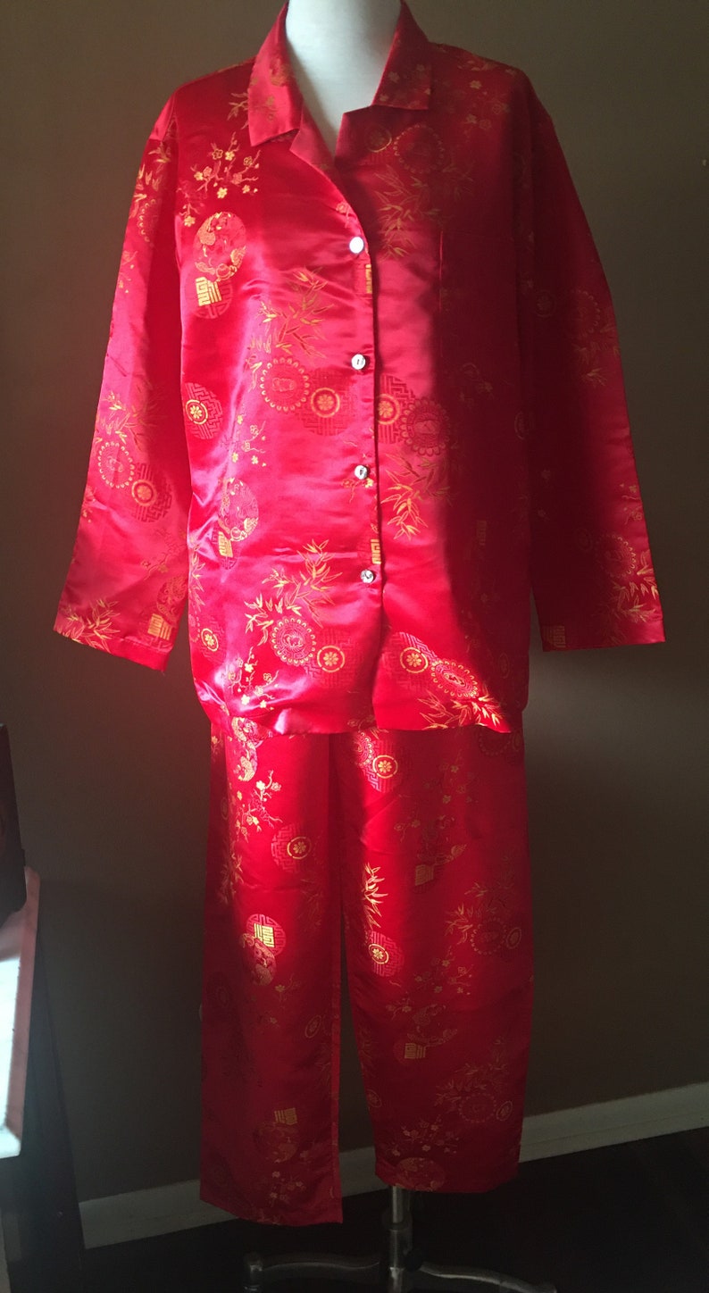 May include: Red pajama set with a gold floral pattern. The set includes a button-down shirt and matching pants. The fabric has a satin sheen. The pajamas are displayed on a mannequin.