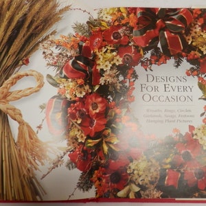 May include: A book titled "Designs for Every Occasion" with a red and green wreath on the cover. The wreath is made of red flowers, green leaves, and red and green ribbon. The book also features a close-up of a bundle of wheat tied with a rope.