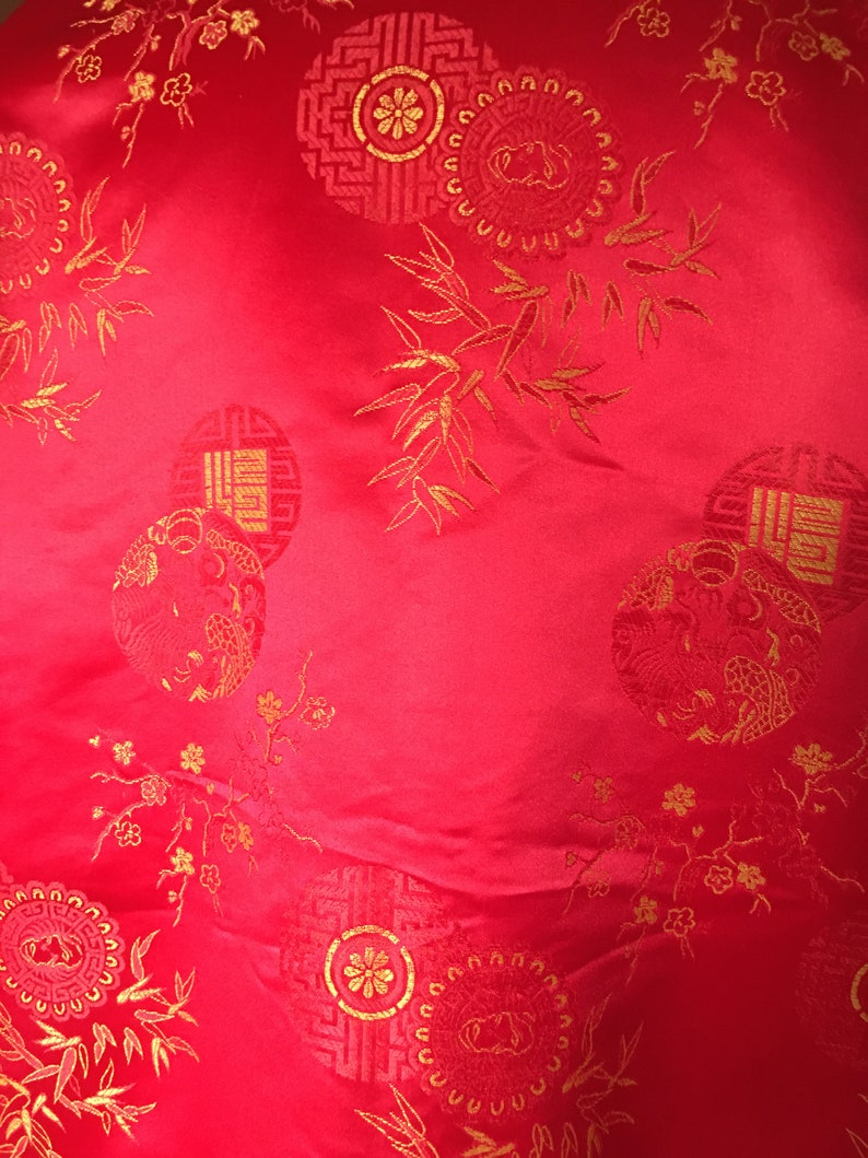 May include: Bright red fabric with gold embroidered circular patterns and floral and bamboo accents. The design includes detailed medallions and stylized botanical elements, creating a rich, textured appearance. The fabric has a slight sheen.