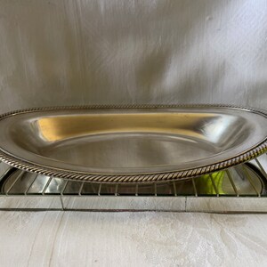 May include: A silver oval serving platter with a rope-like design around the edge. The platter is sitting on a mirrored surface.