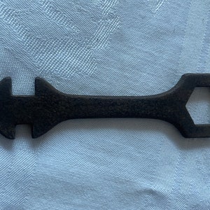 Könnte beinhalten: Ein schwarzer Schraubenschlüssel aus Metall mit einem sechseckigen Kopf und einem spitzen Ende. Der Schraubenschlüssel ist zum Anziehen und Lösen von Muttern und Schrauben gedacht.