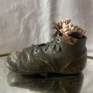 May include: A vintage black leather boot with pink floral accents, repurposed as a planter. The boot is worn and has a distressed look.