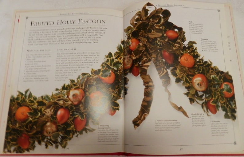 May include: A close-up of a fruited holly festoon, a Christmas decoration made with holly leaves, red berries, and apples. The festoon is tied together with a brown ribbon. The text "Fruited Holly Festoon" is visible in the image.