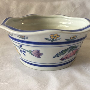May include: White ceramic bowl with a scalloped rim, adorned with blue stripes and floral patterns in yellow and pink. The bowl has a blue trim and is suitable for decorative or functional use.