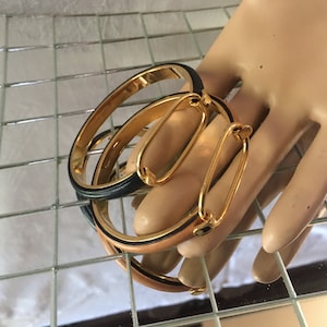 May include: Two gold-toned bracelets with black and tan leather bands. The bracelets are stacked on top of each other and have a gold clasp.