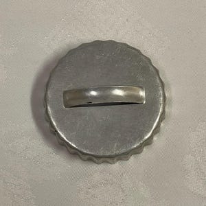 May include: A round, silver-colored cookie cutter with a scalloped edge and a rectangular handle. The cutter is made of metal and appears to be vintage or antique. The design is simple and functional, suitable for baking.