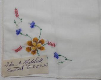 May include: White linen handkerchief with embroidered flowers in shades of pink, blue, yellow, and green. The handkerchief has a handwritten label that reads "Ida A. Mickoll Newark O. 1-27-52".