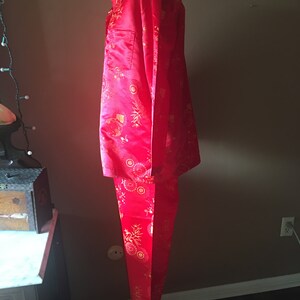May include: A red pajama set with a gold floral pattern. The set includes a collared, button-down shirt with a chest pocket and matching pants. The fabric has a satin sheen.