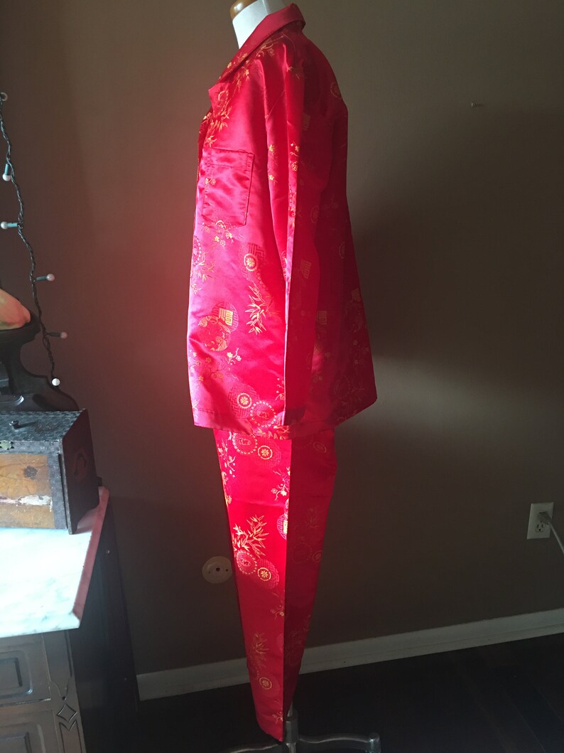 May include: A red pajama set with a gold floral pattern. The set includes a collared, button-down shirt with a chest pocket and matching pants. The fabric has a satin sheen.