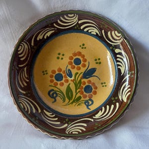 Puede incluir: Un plato de cerámica amarillo con un borde marrón y un diseño floral en tonos naranja, azul y verde.