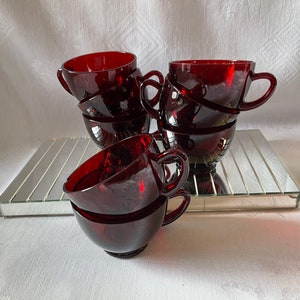 Könnte beinhalten: Ein Satz von sechs roten Glasbechern, die auf einer verspiegelten Oberfläche gestapelt sind. Die Becher sind alle gleich groß und gleich geformt und haben einen abgerundeten Boden und einen breiten Rand.