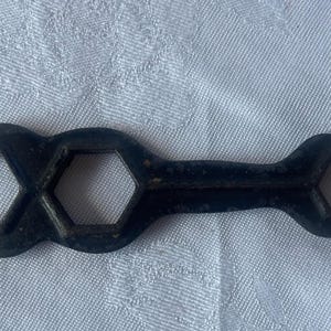 Könnte beinhalten: Ein schwarzer Schraubenschlüssel aus Metall mit zwei offenen Enden und einem sechseckigen Loch in der Mitte.