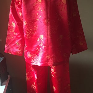 May include: A red pajama set with a matching button-down shirt and pants. The set features a gold floral and geometric pattern. The fabric has a slight sheen, and the outfit is displayed on a mannequin.