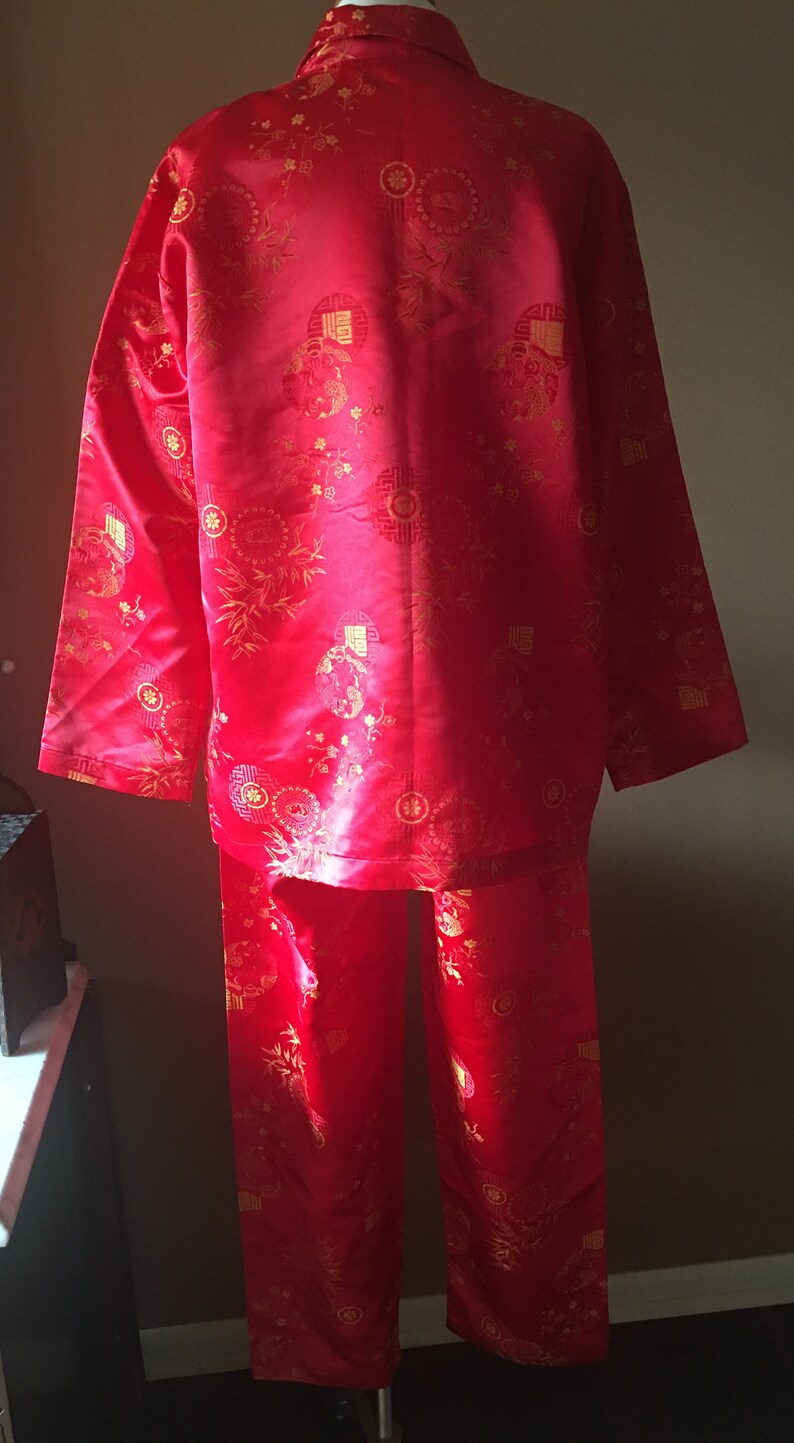 May include: A red pajama set with a matching button-down shirt and pants. The set features a gold floral and geometric pattern. The fabric has a slight sheen, and the outfit is displayed on a mannequin.