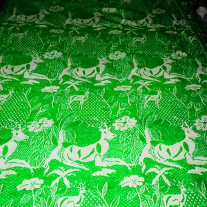 May include: A green and white woven blanket with a repeating pattern of deer and floral designs.