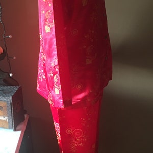 May include: Red pajama set with a button-down shirt and matching pants. The set features a gold floral and character pattern. The fabric has a slight sheen. The pajamas are displayed on a mannequin.