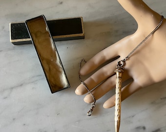 May include: A gold-toned pencil with a chain attached to it. The pencil is in a black box with a white interior. The pencil has a diamond pattern on it.