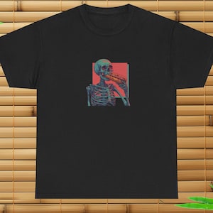 May include: A black t-shirt featuring a graphic of a skeleton eating a hot dog. The skeleton is blue and green, and the hot dog is yellow and red. The graphic is surrounded by a red and pink rectangle.