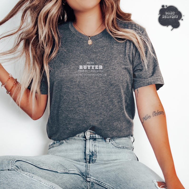 Puede incluir: Camiseta gris oscuro con la palabra "BUTTER" impresa en blanco. El texto est&aacute; centrado y acompa&ntilde;ado de las palabras "SALTED" y "GRADE AA". La camiseta es de color gris jaspeado.