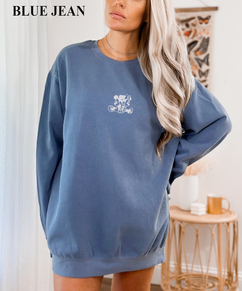 May include: Blue jean colored sweatshirt with a small white graphic on the chest. The sweatshirt has a crew neck and long sleeves. The text "BLUE JEAN" is at the top of the image.