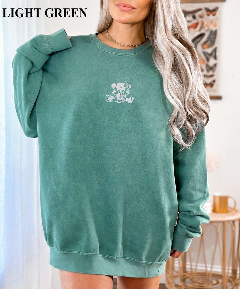 May include: Light green sweatshirt with a crew neck and long sleeves. The sweatshirt features a small, white graphic of cartoon characters on the front. The text "LIGHT GREEN" is at the top of the image.