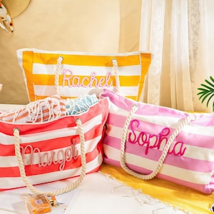 Könnte beinhalten: Drei gestreifte Strandtaschen in Gelb, Rosa und Koralle mit weißen Streifen. Jede Tasche hat einen Seilgriff und einen Namen auf der Vorderseite: Rachel, Sophia und Margot. Die Taschen sind offen und zeigen den Inhalt.