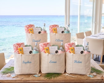May include: Five beige canvas tote bags, each personalized with a name in blue embroidery. Inside each bag are a coral-patterned towel, a yellow sunscreen tube, a glass water bottle, a small tumbler, a pair of sunglasses, and a Thank You card.