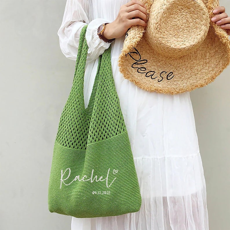 May include: A green knitted tote bag with a wide shoulder strap. The bag has the name "Rachel" embroidered in white script, along with a date. A straw sun hat with the word "Please" embroidered on the brim is held nearby.