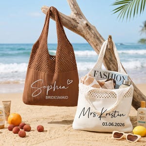 May include: Two beach tote bags, one brown and one white, are on a sandy beach. The brown bag has the name "Sophia" and "Bridesmaid" printed on it. The white bag has "Mrs. Kristin" and the date "03.06.2026" printed on it. Beach accessories are scattered around.