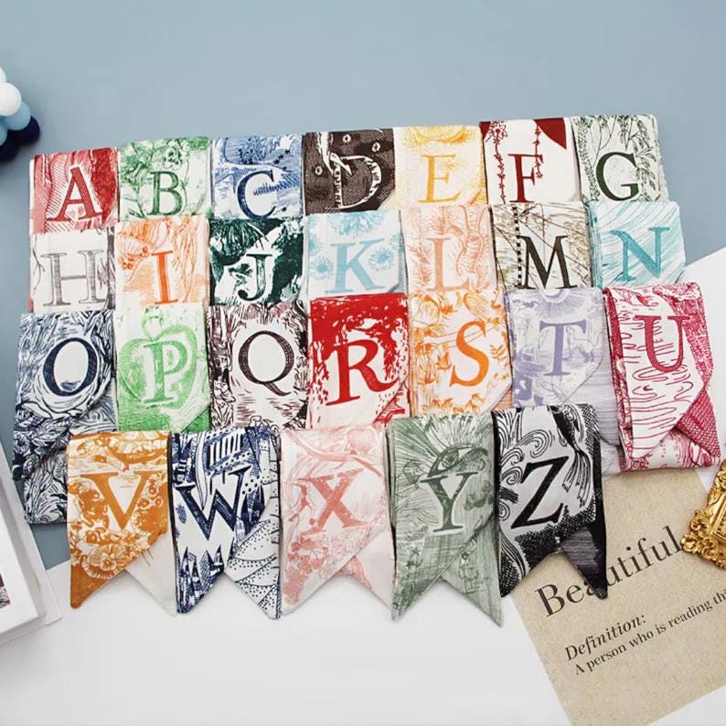 May include: A set of 26 fabric alphabet flags with colorful backgrounds and vintage-style letter designs. Each flag is folded in half to create a triangular shape. The flags are arranged in alphabetical order from A to Z.